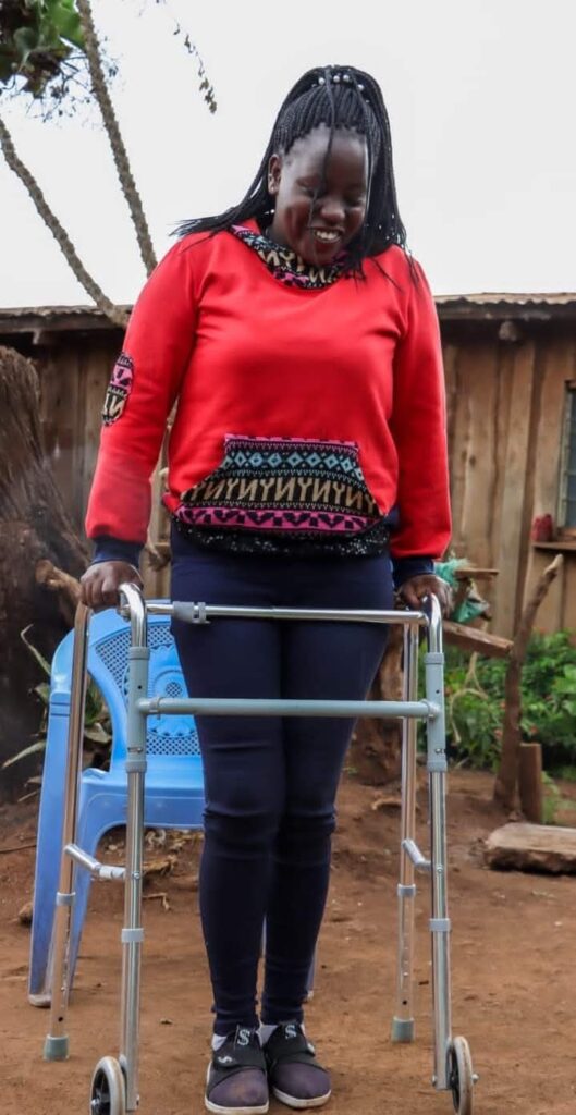 Lucy Mueni, standing using a walking frame. In her mind, she believes this is just a phase... It will pass